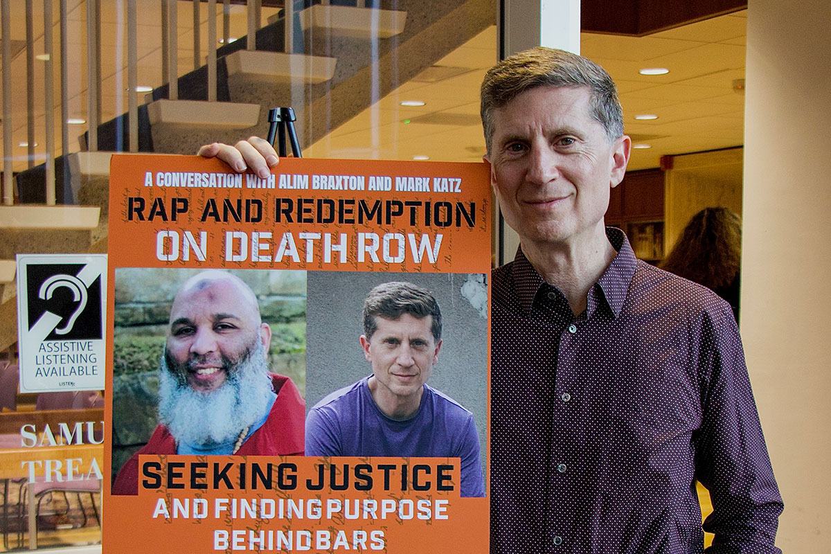 Mark Katz standing next to the event poster for the "Rap and Redemption on Death Row" presentation.